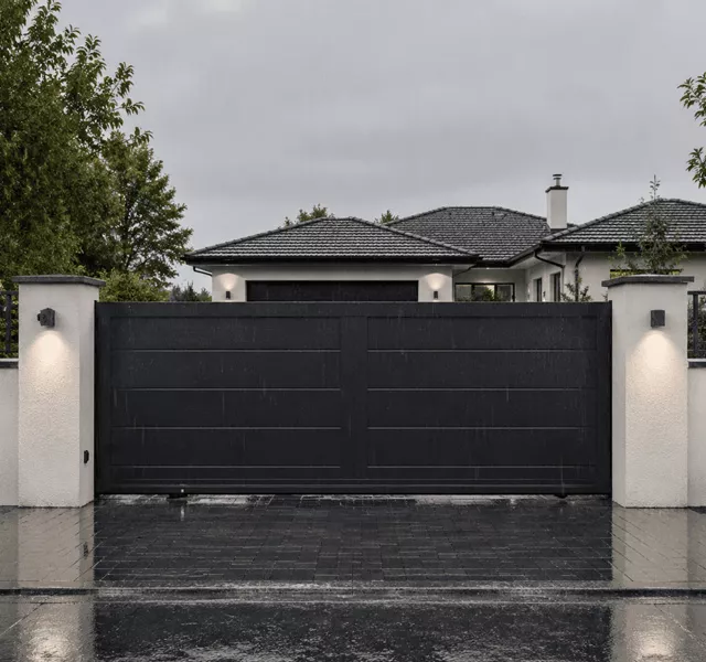 Portail noir fermé devant une maison moderne sous la pluie avec allée mouillée